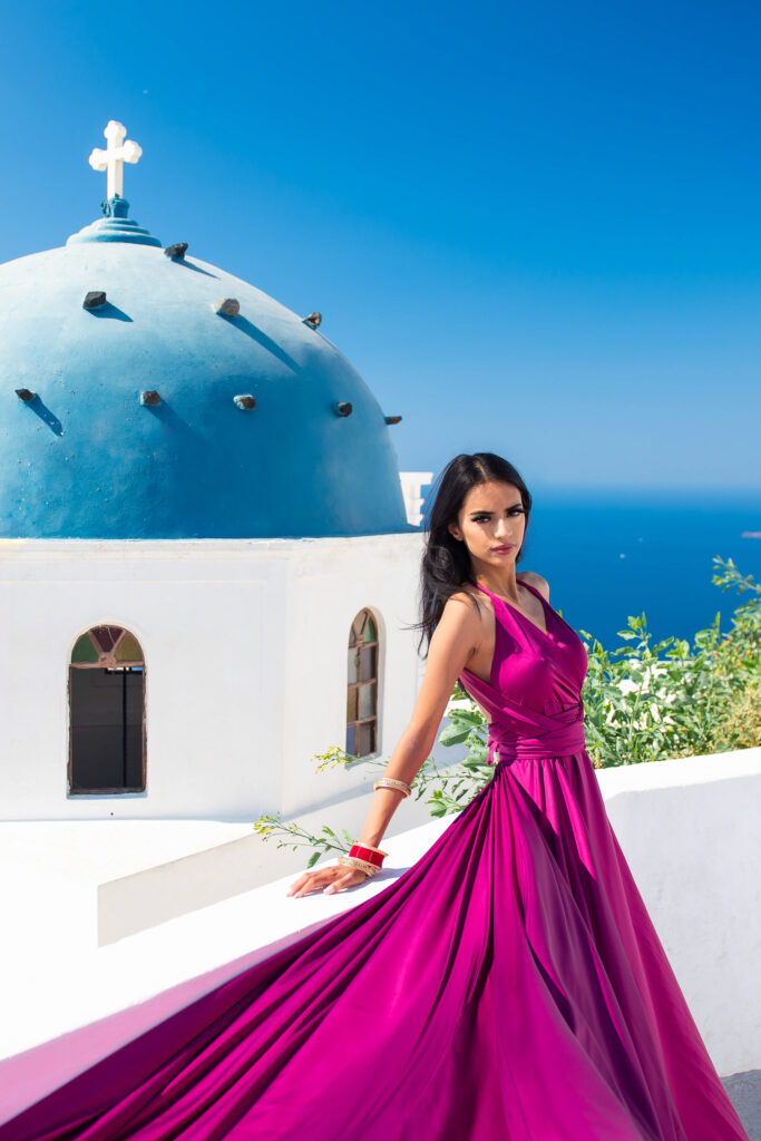 Woman posing in a purple flying dress beside a blue-domed church in Santorini