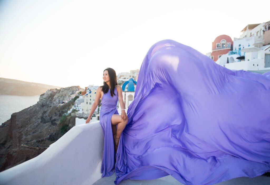 Woman seated in a lavender flying dress with its train flowing over the Santorini caldera