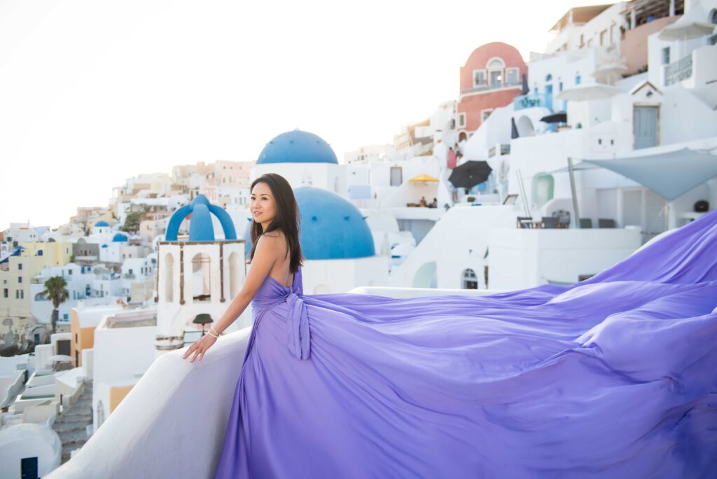 Woman stading in a lavender flying dress with Oia’s blue-domed churches behind her