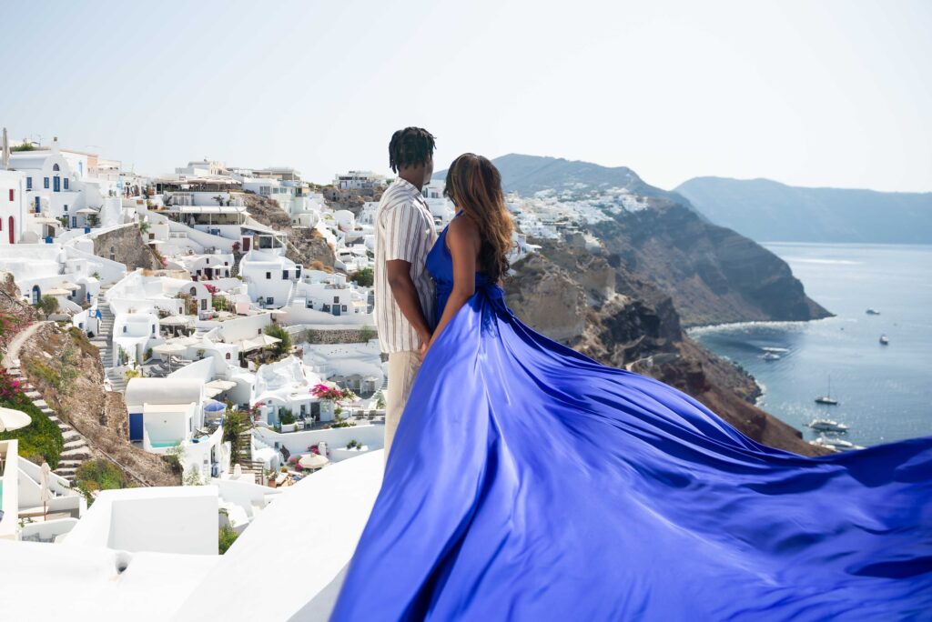 Couple embracing as a royal-blue flying dress flows across a Santorini rooftop