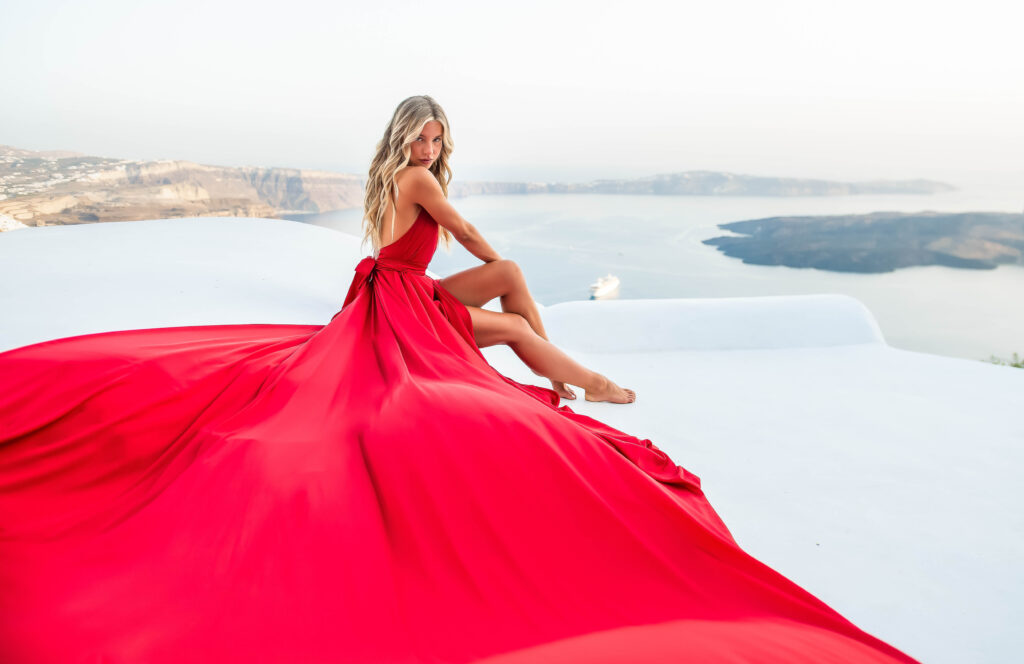 Blonde woman seated on a white rooftop with a red flying dress spread around her