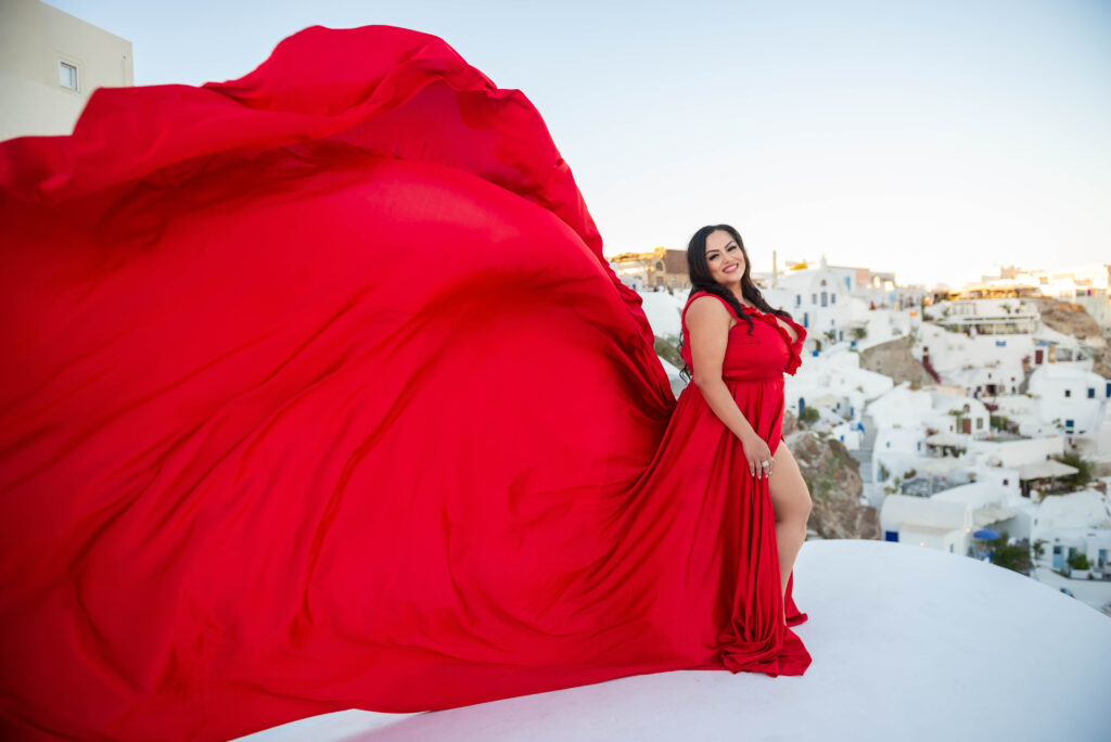 A woman enjoying the beautiful Oia sunset in Santorini, smiling while wearing a stunning white ruffled dress that flows in the wind.