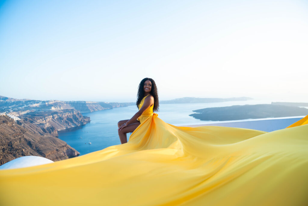 A lady stands on the edge of a rooftop in Santorini, overlooking a breathtaking view of the sea, with a joyful expression on her face as she laughs at the moment. The combination of the scenic view and the lady's carefree laughter creates a sense of freedom and happiness.
