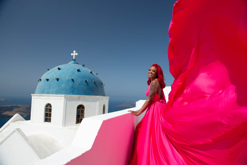 A lady with pink hair laughs joyfully, with the bright blue sky in the background on a beautiful, sunny day. The combination of her vibrant hair color and the stunning scenery creates a sense of playfulness and happiness, making for a delightful image.