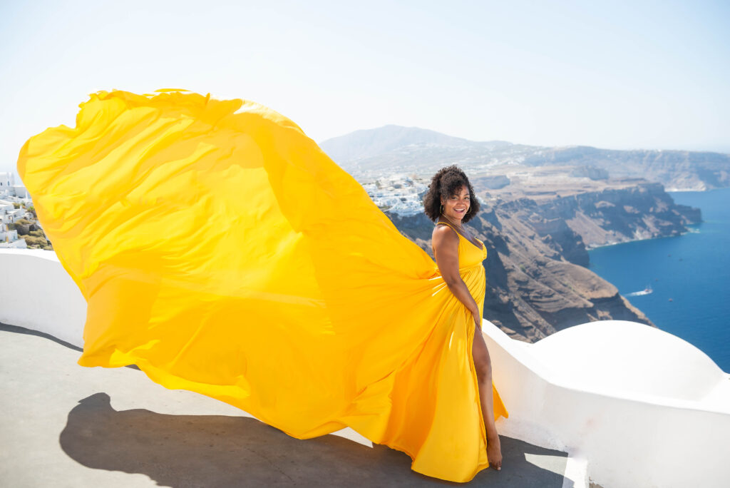 A joyful lady, wearing a bright yellow flying dress, bursts into laughter against the stunning backdrop of white rooftops. Her infectious laughter captures the carefree and playful spirit of the moment, creating a sense of warmth and happiness.