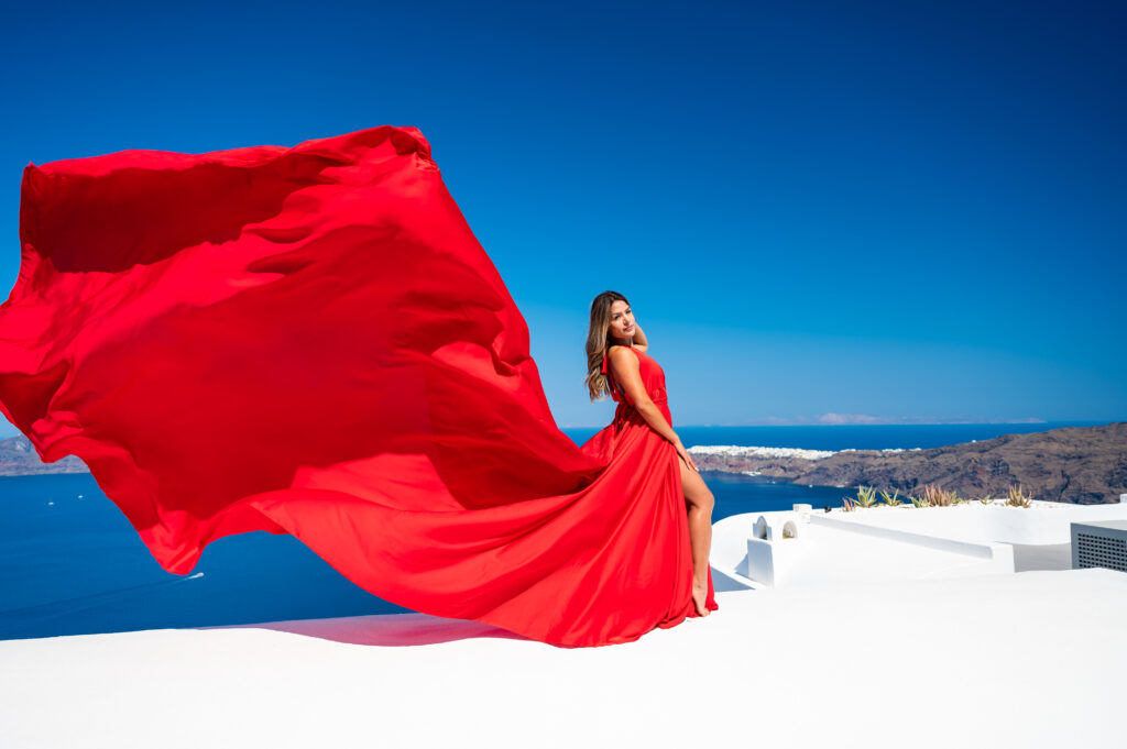 A woman with an elegant and charming demeanor posing for the camera while wearing a beautiful red dress. She is standing upright, and her arms are relaxed by her side, with a confident and friendly expression on her face.