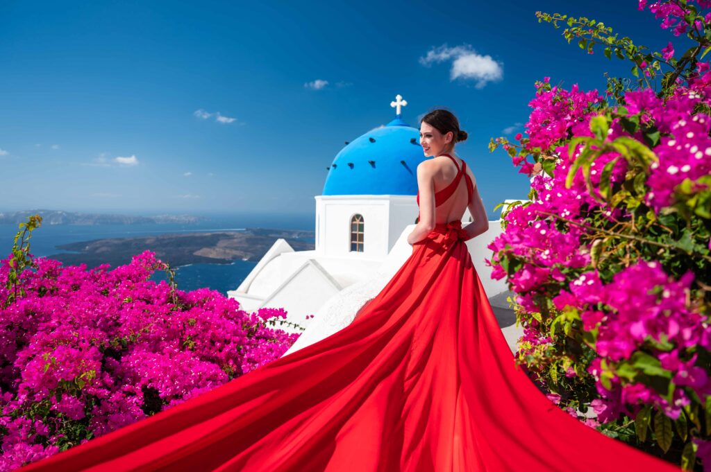 A dreamy image of a woman wearing a red dress and holding it up, as if about to take flight, amidst the idyllic scenery of Santorini
