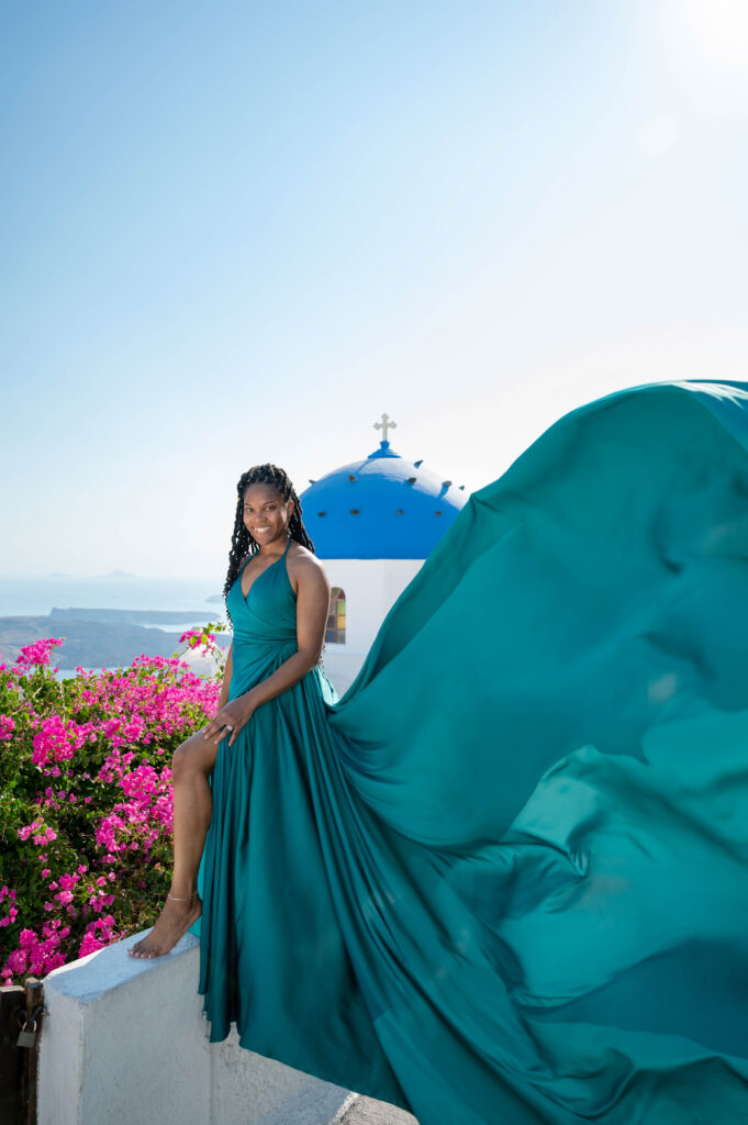A graceful woman in a vibrant dress poses in mid-air as she gazes out at the stunning Santorini coastline.