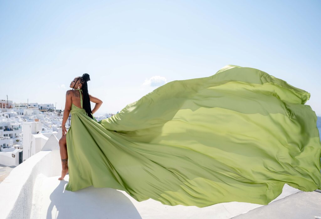 Woman looking over her shoulder in an olive-green flying dress above Santorini’s whitewashed rooftops