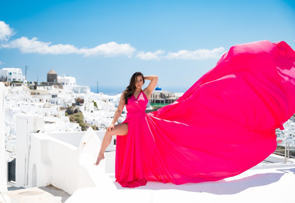 Woman in fuchsia flying dress standing on a rooftop in Santorini.