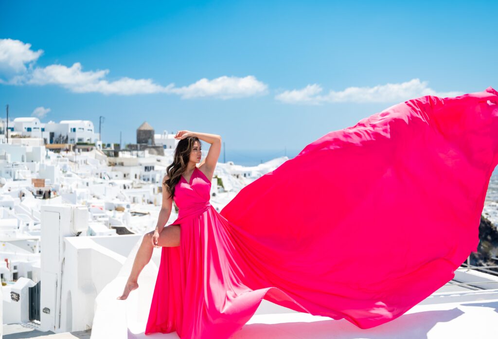 Model posing in fuchsia flying dress with Santorini caldera in the background.