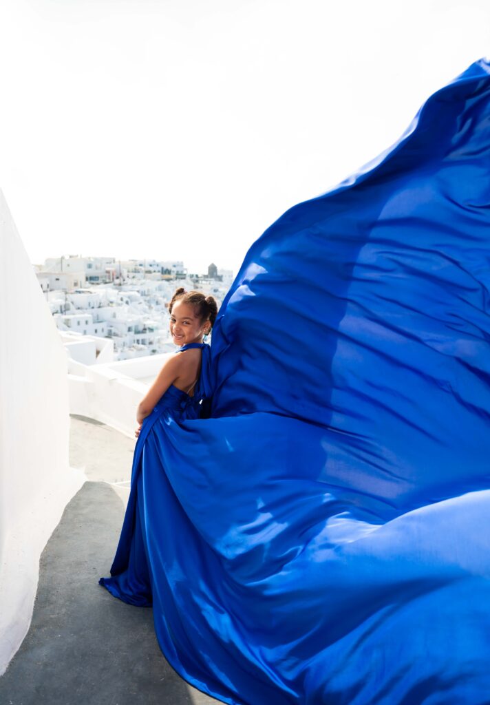 Young girl in blue flying dress standing on Santorini steps with cave houses view