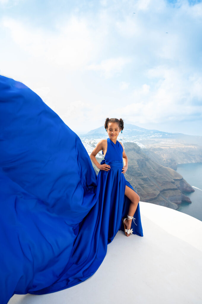 Child in a flowing blue flying dress enjoying a Santorini photoshoot