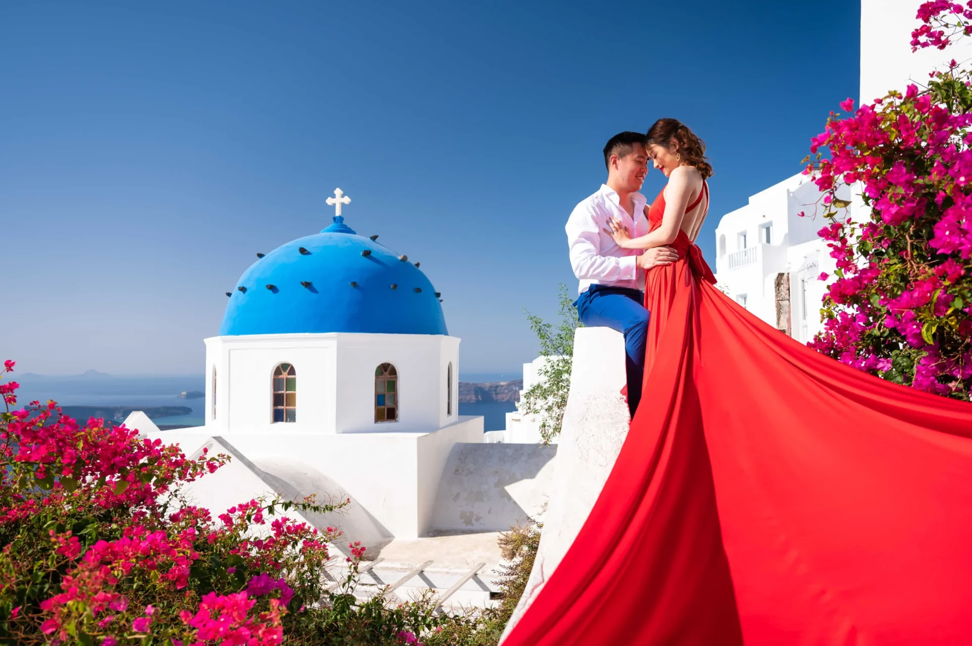 Couple touching foreheads during a Santorini photoshoot with blue domes church view and flowers