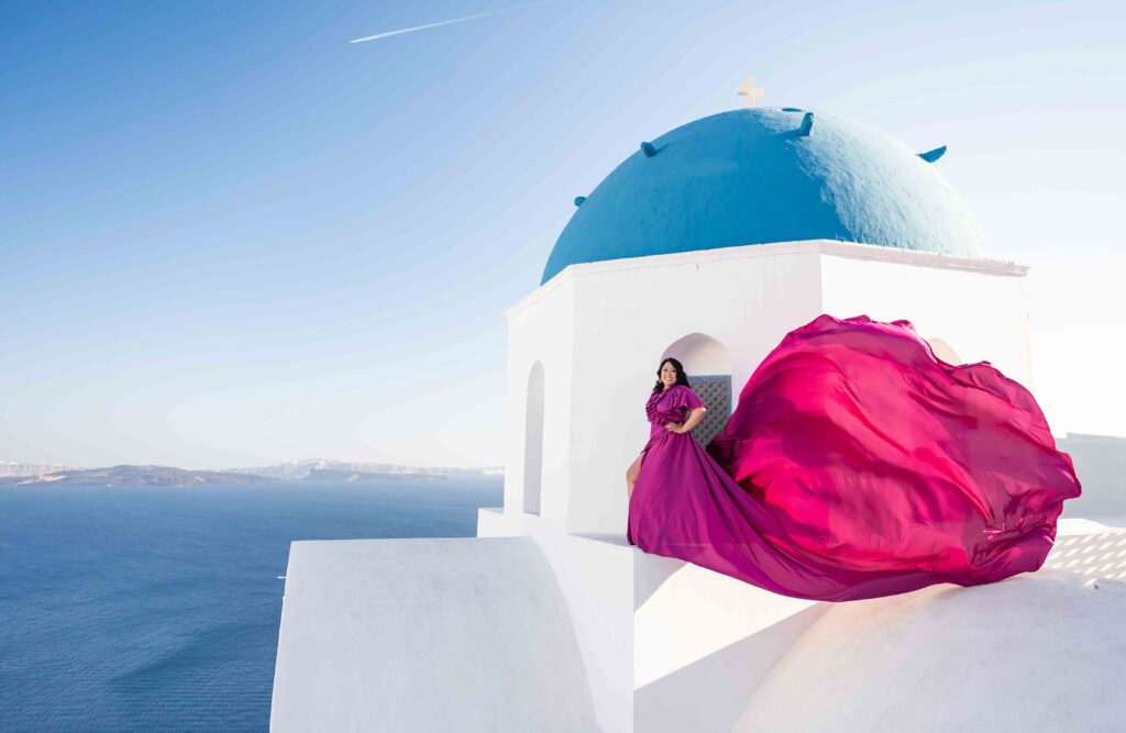 A female is posing with a smile a top of the blue domes chapel in purple ruffles flying dress