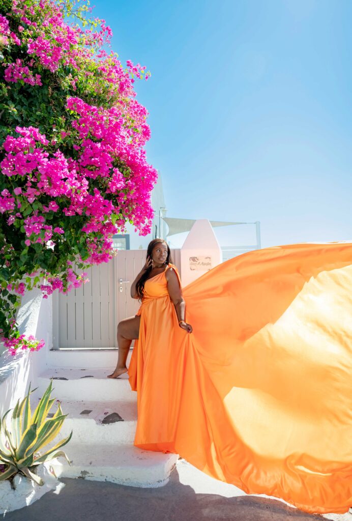 Lady standing on a stair while looking away, in the back we see Aegean sky and flowers
