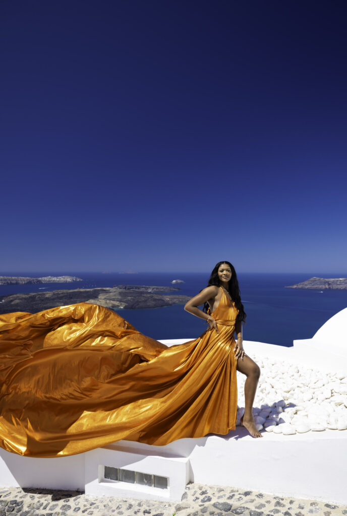 A lady getting a photographed with a high ground sea view and white cave buldings.