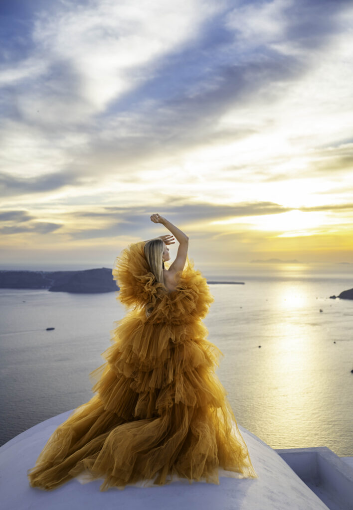 A lady with her hand extended in the air looking down the sunset and sea view