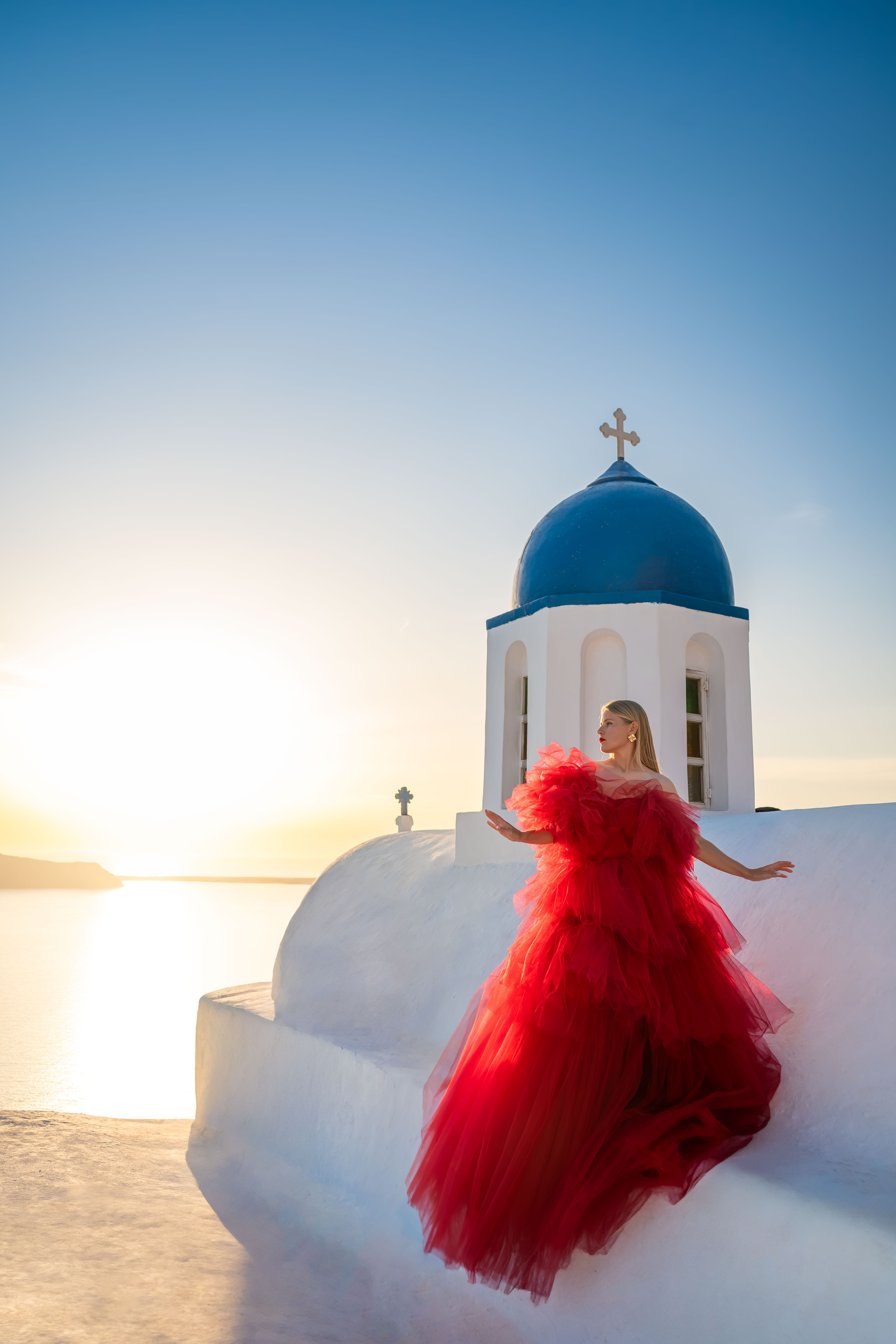 Girl getting photographed on top of a Santorini church wearing red