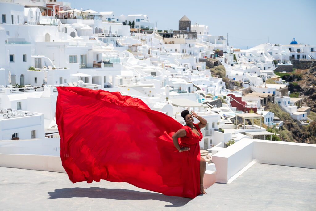 Model in a pose with hand on hair and smiling wearing red ruffles flying dress.