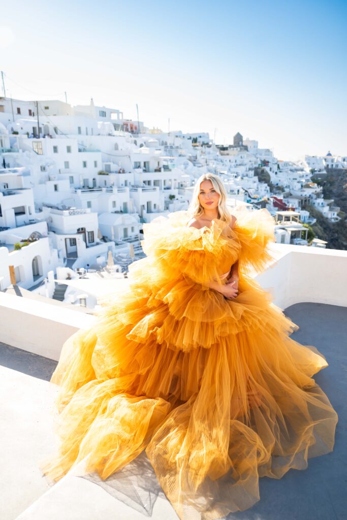 Blue-eyed woman posing in Santorini while wearing an orange fluffy dress.